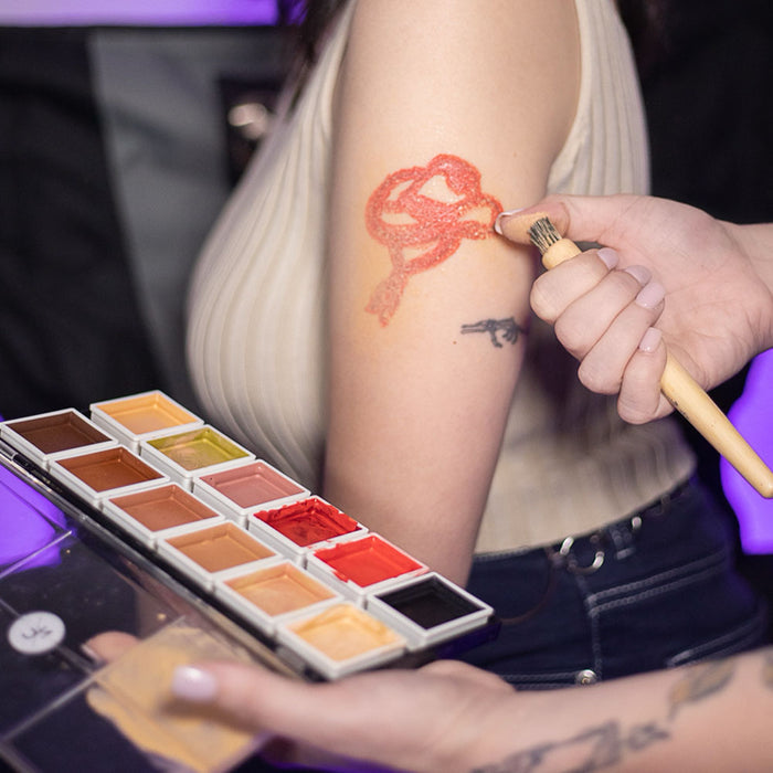 Makeup artist applying 12-Color Tattoo Cover-Up Palette to client's arm tattoo