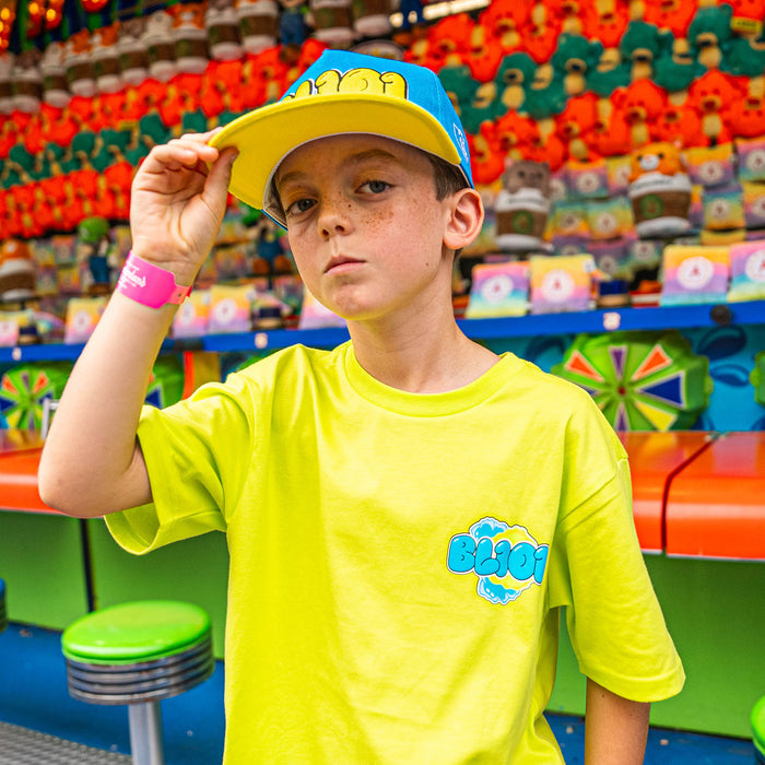 Young boy wearing a yellow and blue BL101 cap and shirt with a toy store in the background