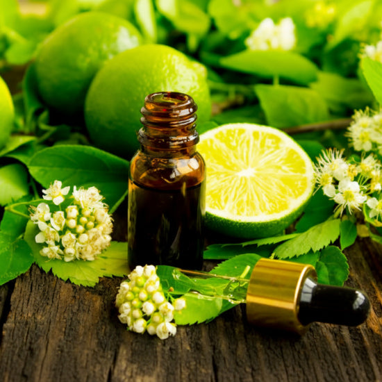 Bottle of essential oil with lime and flowers on a wooden surface