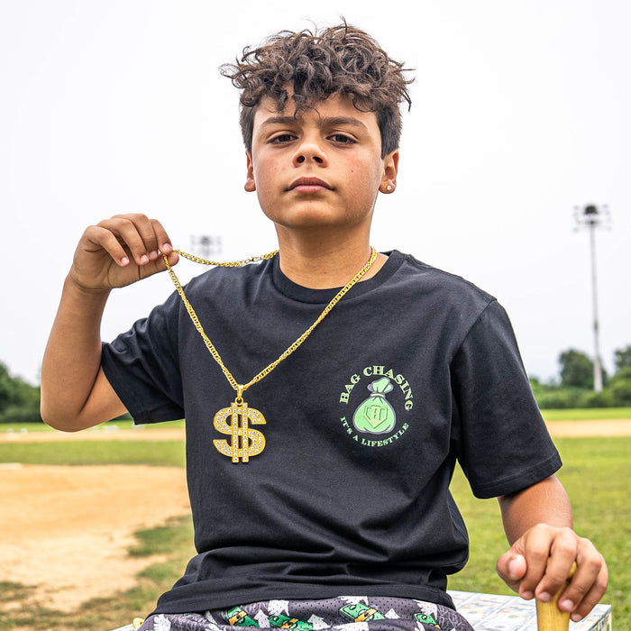 Child holding a gold chain with a dollar sign pendant on a sports field