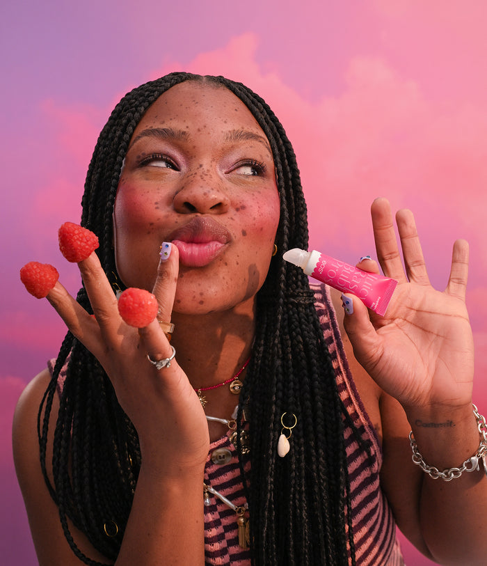 Woman holding strawberries and a small pink object against a pink and purple gradient background