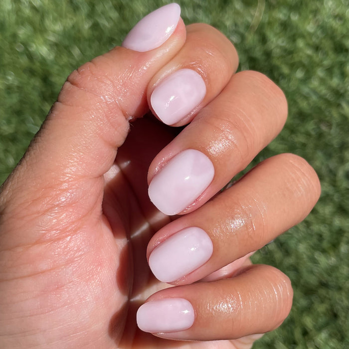 Hand displaying Strawberry Scone - Press-On | XS | Round with extra-short, glossy, semi-sheer pink false nails manicure style outdoors