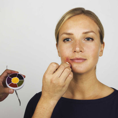 Makeup artist applying mouth-corner bruise SFX to model using 6 Color Bruise Wheel and metal applicator