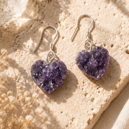 Heart-shaped purple druzy earrings on a beige stone surface