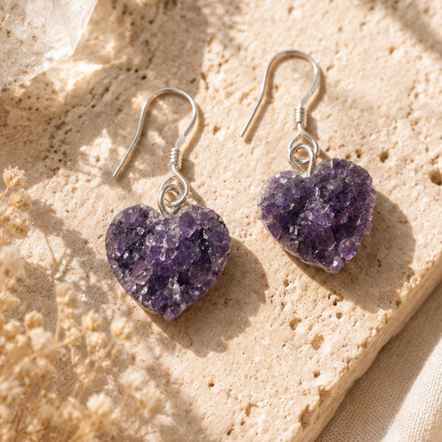 Heart-shaped purple druzy earrings on a beige stone surface
