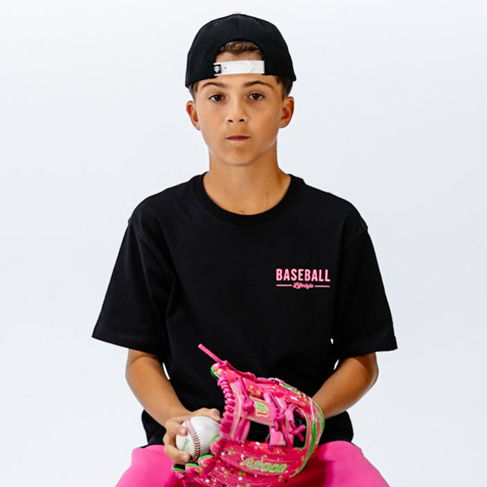 Child wearing a black t-shirt with pink 'BASEBALL Lifestyle' text in top corner, holding a pink baseball glove and ball on a white background