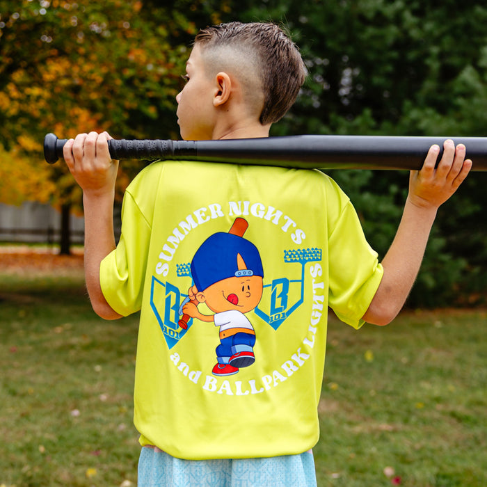 Child wearing a bright yellow shirt with Pablo Sanchez on the back and 'Summer Nights and Ballpark Lights' text, holding a baseball bat outdoors.