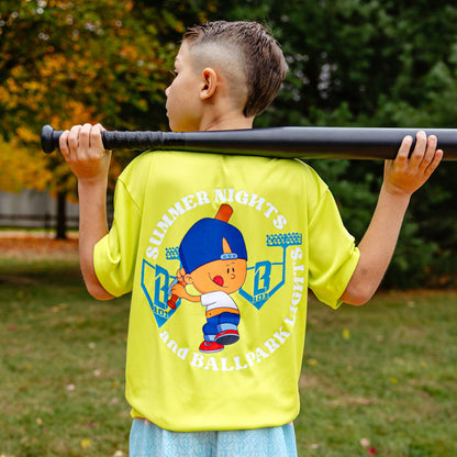 Child wearing a bright yellow shirt with Pablo Sanchez on the back and 'Summer Nights and Ballpark Lights' text, holding a baseball bat outdoors.