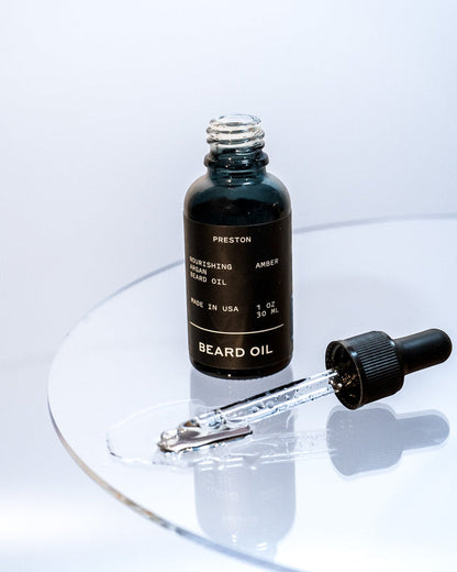 Amber beard oil bottle with dropper releasing oil onto surface