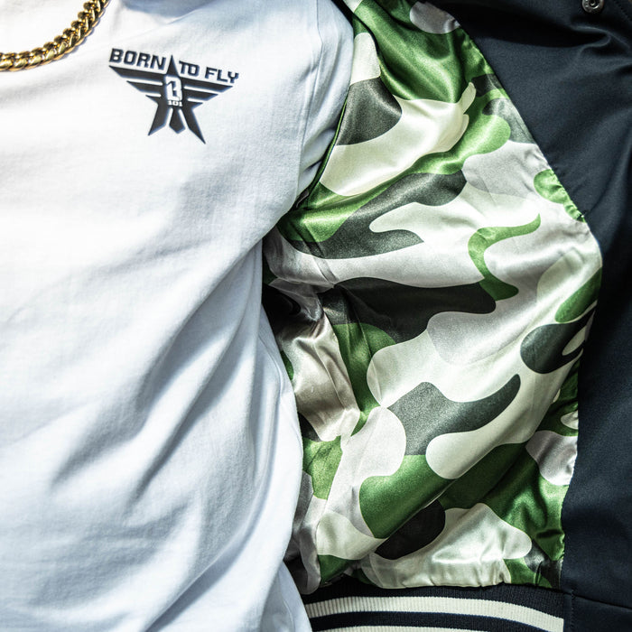 Close up of Youth white t-shirt with black “BORN TO FLY” lettering, black star, and white BL101 logo inside the star positioned on the top corner of the shirt on person