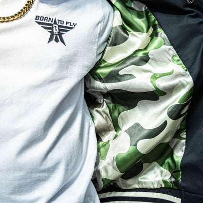 Close up of Youth white t-shirt with black “BORN TO FLY” lettering, black star, and white BL101 logo inside the star positioned on the top corner of the shirt on person