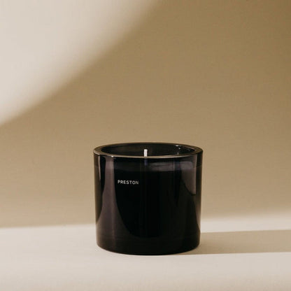 Black 7 oz scented candle jar with lit wick and 'PRESTON' label on front