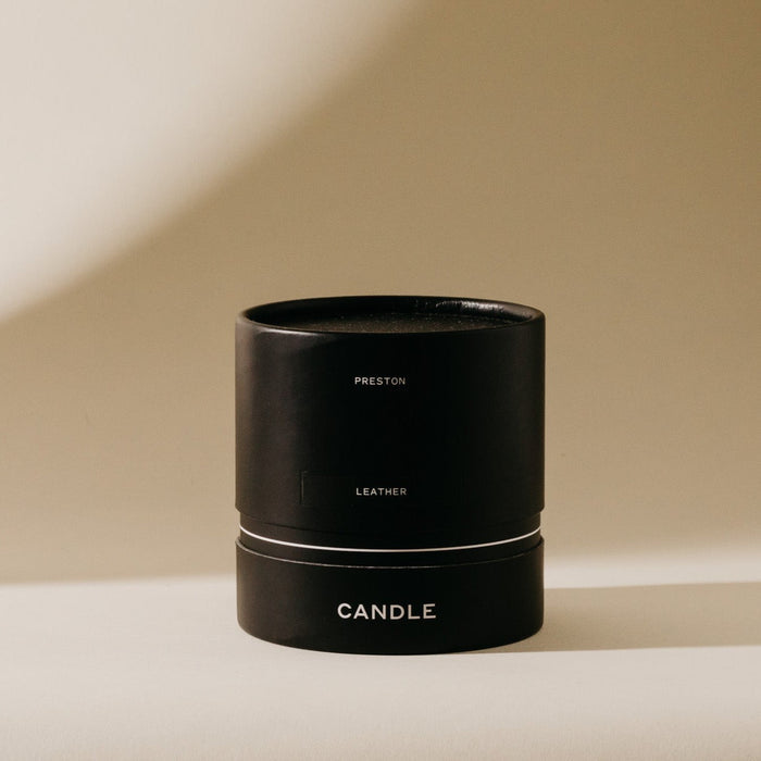 Black 7 oz scented candle with 'LEATHER' and 'CANDLE' text on front band