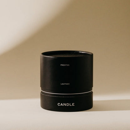 Black 7 oz scented candle with 'LEATHER' and 'CANDLE' text on front band
