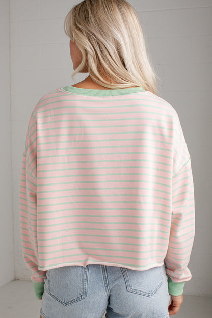 A woman viewed from behind wearing a light pink and white striped long-sleeve crop top with sage green ribbed trim, paired with light blue jeans.