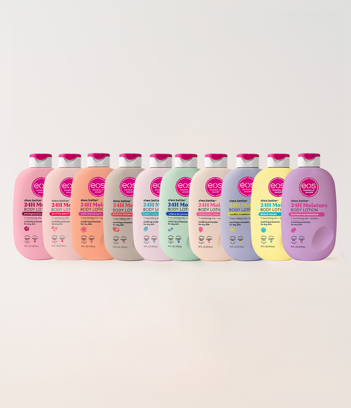 A row of ten eos Body Lotion bottles in assorted pastel colors, including pink, peach, gray, mint, lavender, and yellow, arranged against a light beige background.