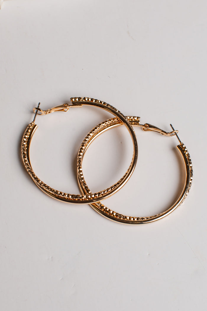 A pair of gold-tone hoop earrings with a textured, beaded outer edge and solid inner bands, displayed on a clean white background.