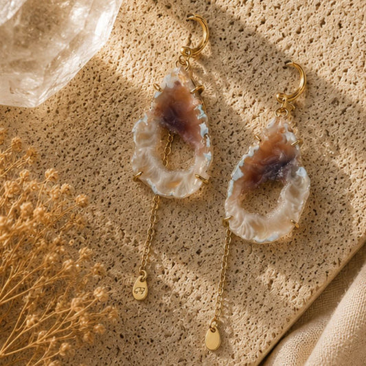 Pair of earrings with agate-like stones on a textured surface with dried flowers.