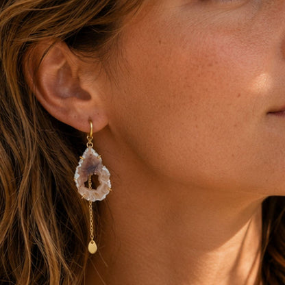 Close-up of a woman wearing a gold earring with a dangling gemstone.