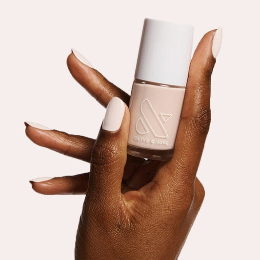 Hand with LHG neutral nail polish on neatly manicured nails holding a matching Olive and June polish bottle