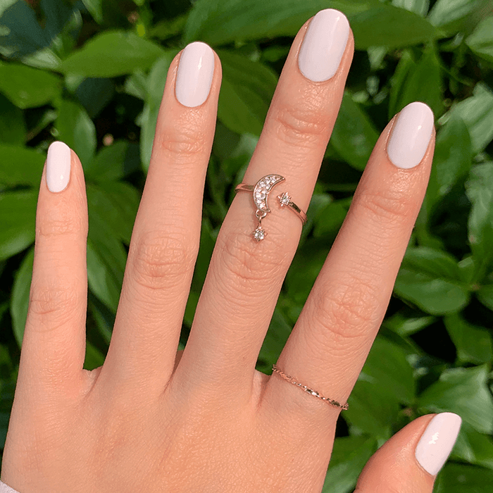 Hand with LHG neutral polish featuring a subtle pink tint on neatly manicured nails against a leafy green background