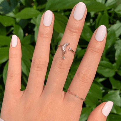 Hand with LHG neutral polish featuring a subtle pink tint on neatly manicured nails against a leafy green background
