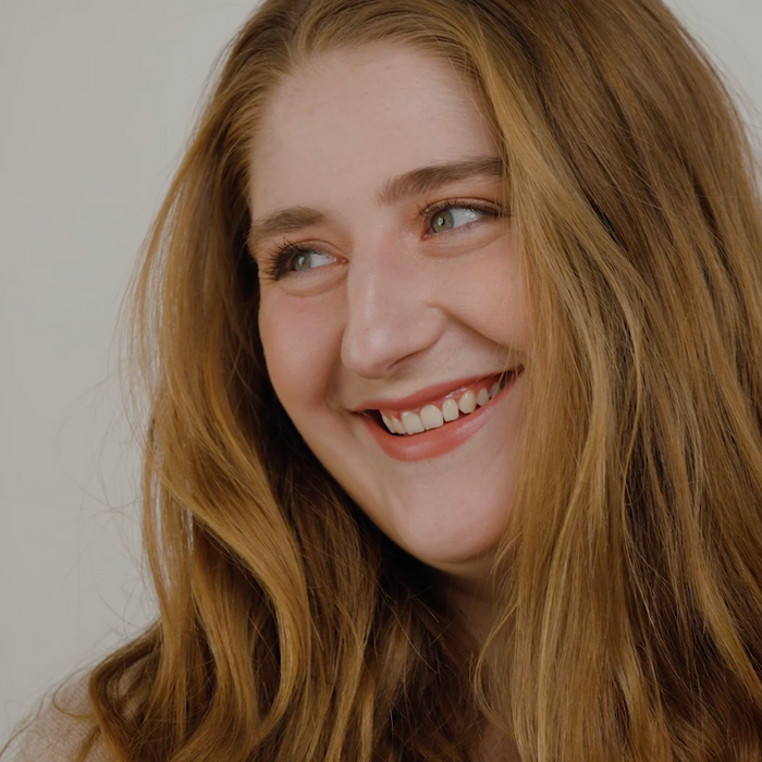 Woman with long, wavy hair smiling against a plain background