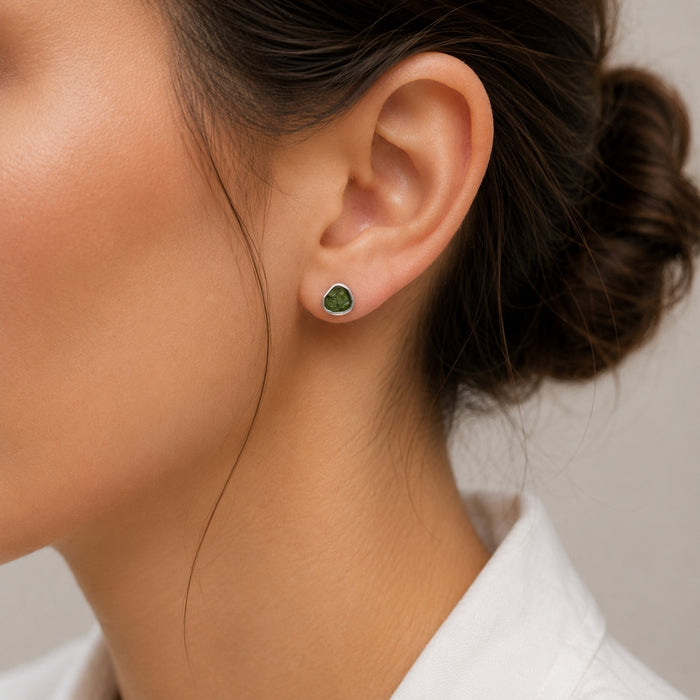 A close-up of a woman's ear wearing a Moldavite stud earring with a silver-toned setting.