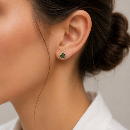 A close-up of a woman's ear wearing a Moldavite stud earring with a silver-toned setting.