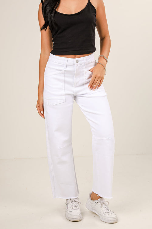 Person wearing a black tank top and white jeans on a beige background