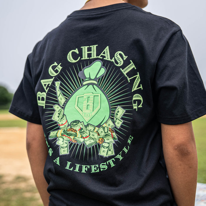 Person wearing a black t-shirt with green money bag graphics and 'Bag Chasing It's a Lifestyle' text on the back.