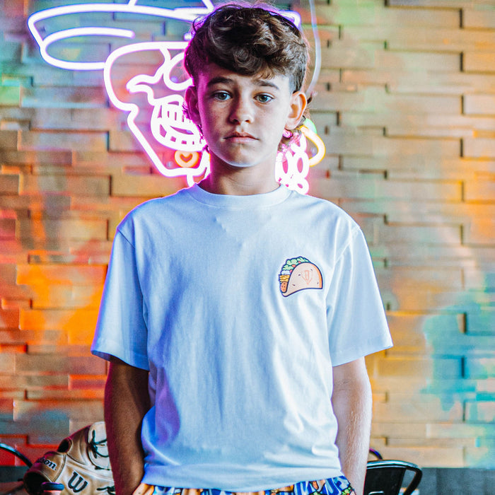 Person wearing a white t-shirt with a taco graphic in front of a colorful neon sign.