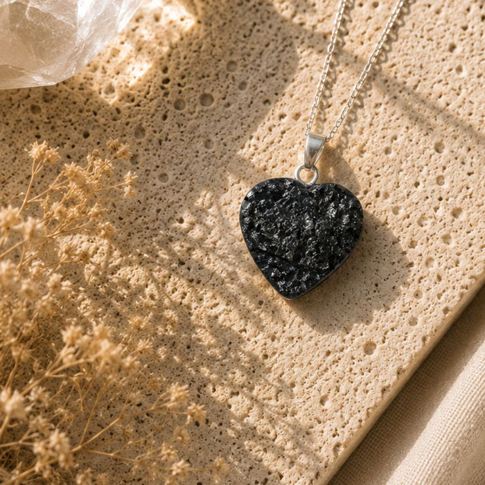 Heart-shaped black stone pendant on a chain against a textured beige surface with dried flowers.