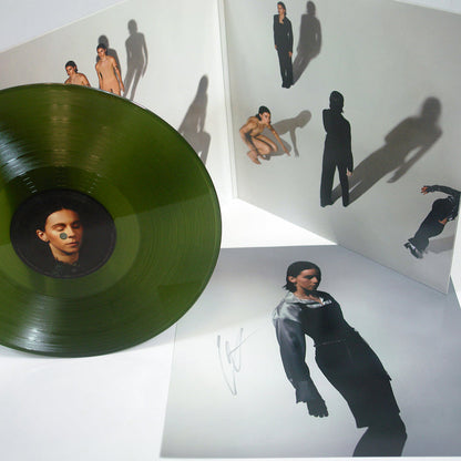 A green PVRIS vinyl record sits beside its open album cover, a signed 12x12 insert, and the tracklisting. Both the cover and insert feature artistic photos of a person posing with bold shadows on a white background.