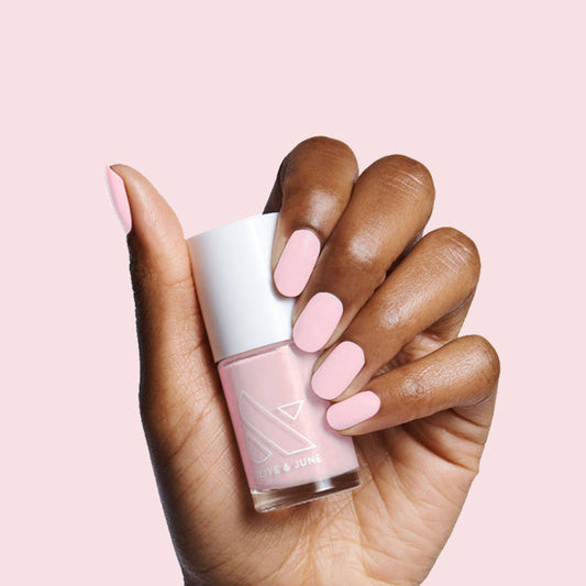 Hand with nails painted in soft rose pink holding Rosy Tips gel polish bottle on light pink background