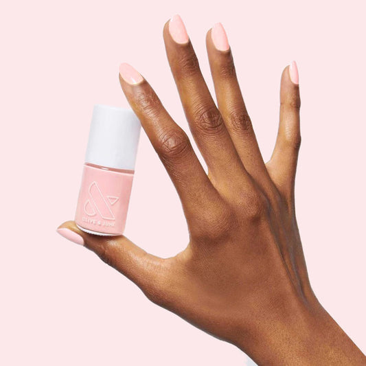 Hand with SCL soft bubblegum pink polish on nails holding a matching bottle against a pale pink background