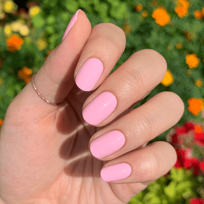 Hand featuring SCL soft bubblegum pink gel polish on nails against a vibrant floral outdoor background