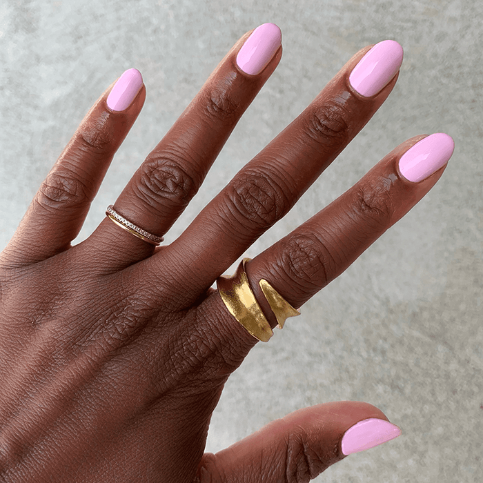 Hand with SCL soft bubblegum pink gel polish on nails adorned with gold rings against a neutral background
