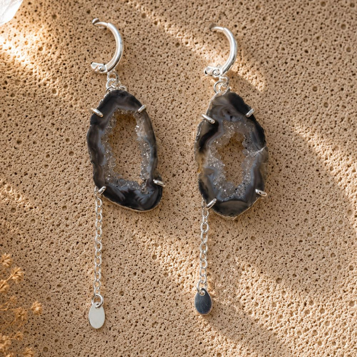Pair of agate stone earrings with silver chains on a textured beige surface