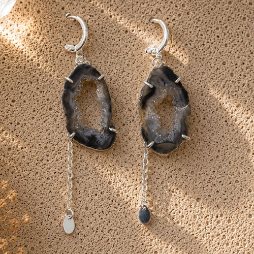 Pair of agate stone earrings with silver chains on a textured beige surface