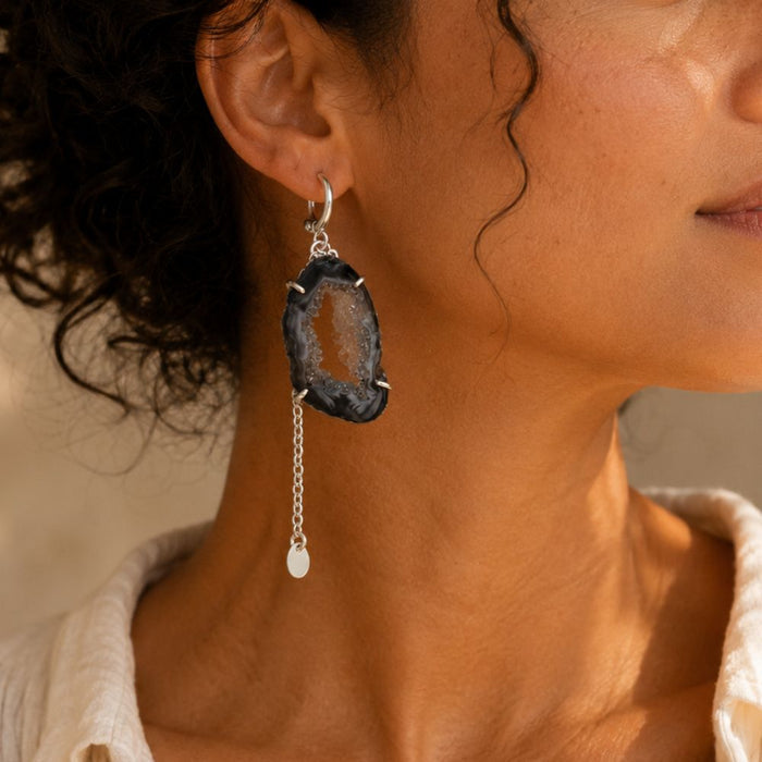 Close-up of a woman wearing a black agate earring with a dangling pearl.