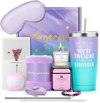A lavender-themed gift set including an eye mask, tumbler, candle, bath bomb, fuzzy socks, bracelet, greeting card, and other self-care items arranged together.