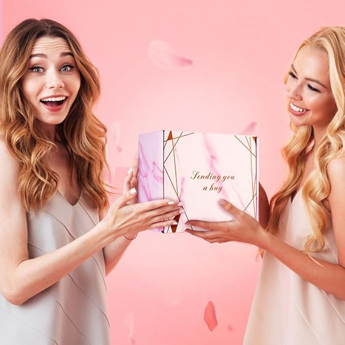 Two smiling women exchanging a pink gift box that says “Sending you a hug” against a soft pink background.