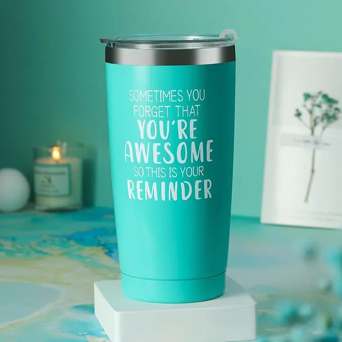 A teal stainless steel tumbler with the motivational quote “Sometimes you forget that you’re awesome so this is your reminder,” placed on a white pedestal with a soft teal background and a lit candle blurred in the distance.