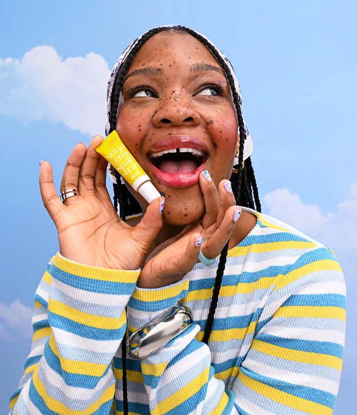 Person holding a tube of lip balm against a blue sky background