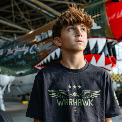 Youth black t-shirt featuring an army green eagle graphic with green “WARHAWK” lettering and a green Armor BL101 logo on person