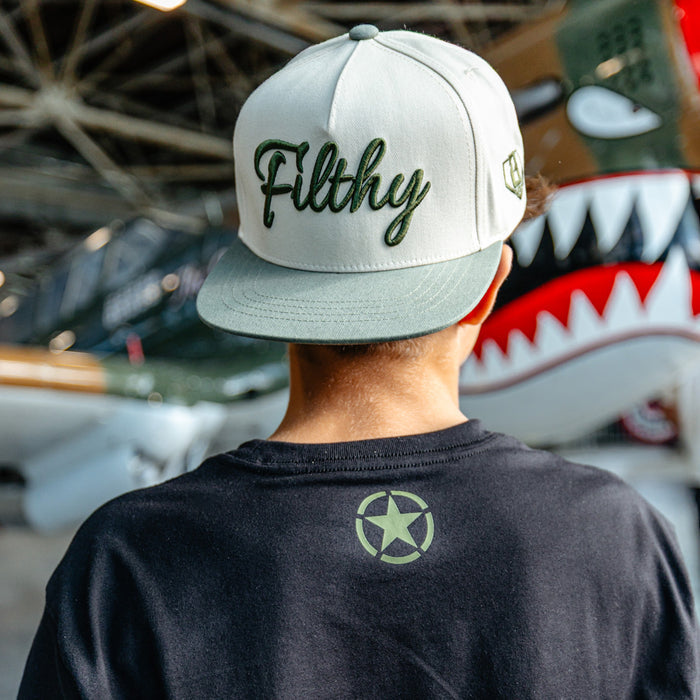 Close up of Youth black t-shirt featuring an army green star graphic and a green Armor BL101 logo on sleeve on person