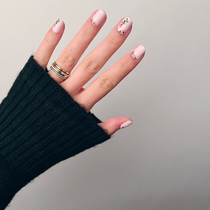 Wild Bouquet - Press-On | Short | Squoval pink short nails with delicate floral and leafy nail art on hand in black sleeve
