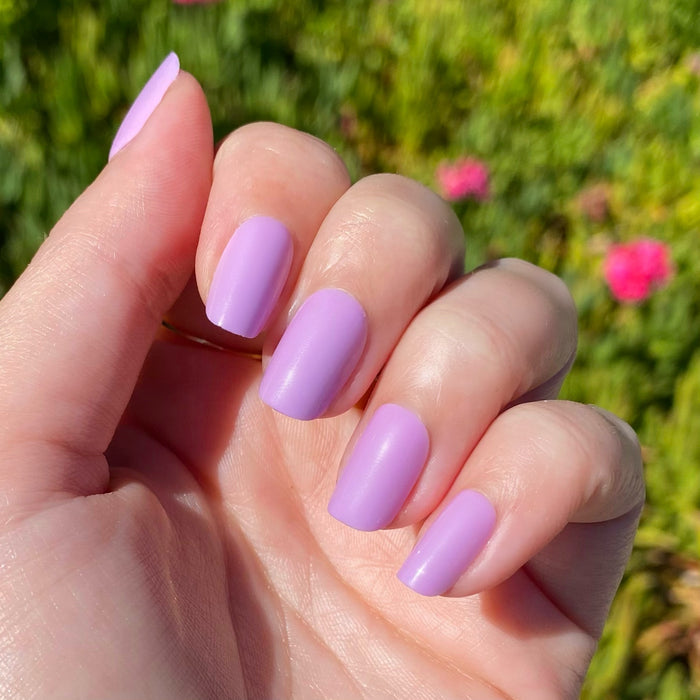 Hand displaying You're Invited - Press-On | Short | Squoval with playful lilac purple short squoval press-on manicure outdoors